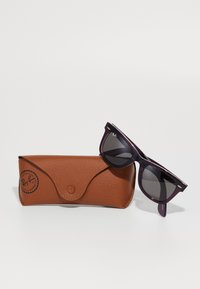 Tamno ljubičaste Ray-Ban Wayfarer naočale za sunce odložene na smešnom smešnom kožnom slučaju smeđe boje s kopčom na dugme i logotipom.