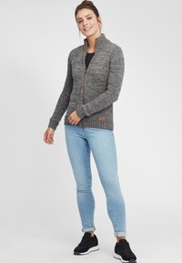 Gray knitted zip-up sweater with a high collar, featuring ribbed cuffs and hem, accompanied by light blue jeans and black sneakers.
