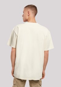 Short-sleeve cream cotton t-shirt with a relaxed fit, round neck, and minimal stitching details, viewed from the back. Casual design.