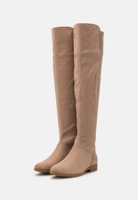 Beige Overknee-Stiefel aus weichem, wildlederähnlichem Material mit einem niedrigen Blockabsatz und einer runden Spitze; glatte Textur, schlichtes Design.