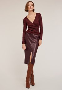 Burgundy texturerad långärmad topp med djup V-ringning, ihopparad med en figurnära brun läder pennkjol med en framslits. Bruna knähöga stövlar.