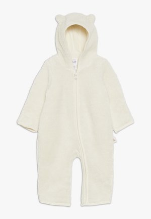 Grenouillère bébé couleur crème, duveteuse, avec capuche, petites oreilles d’ours et fermeture éclair à l'avant.