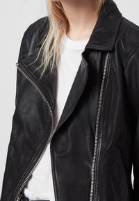 Svart läderjacka med dragkedja framtill, stor krage och sidofickor, med en slät yta och metalliska dragkedjedetaljer.