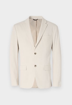 Svijetlosmeđi teksturirani blejzer s jednim gumbom, reverima i dva prednja džepa. Dekorativna šavova i suptilni detalji podstave.