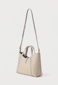 Μπεζ δερμάτινη τσάντα χειρός με διπλές λαβές, ρυθμιζόμενο ιμάντα ώμου και δομημένο σχεδιασμό που διαθέτει τριγωνικό άνοιγμα και διακριτικές ραφές.