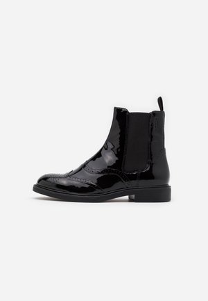 Sorte ankelstøvler i laklæder med elastiske sidestykker, rundet snude og dekorative brogue-detaljer foran. Flad gummisål.