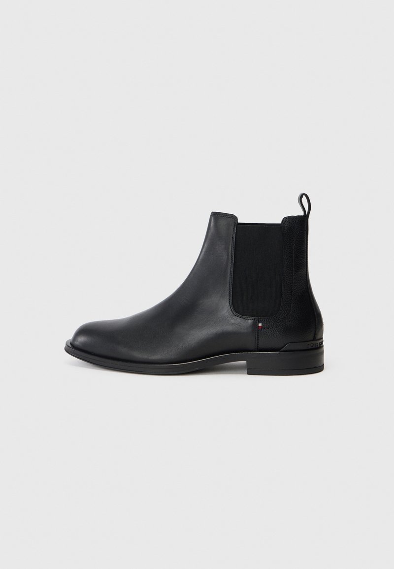 Botín Chelsea de cuero negro con panel lateral elástico y tirador, tacón bajo y punta redondeada suave, sobre un fondo claro y liso.