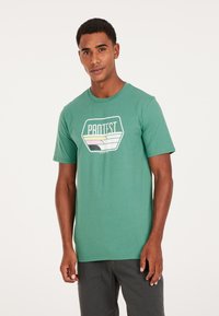Grøn bomulds T-shirt med korte ærmer, med et multicolor "PROTEST" grafisk motiv i en hexagonal design i midten.