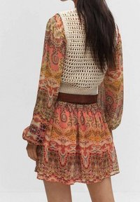 Häkeloberteil in Creme, mit langen gemusterten Ärmeln in Orange, Pink und Gelb mit Paisleymuster. Fließender Rock mit gerafftem Bund und floralen Akzenten.