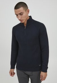 Marinefarbener Reißverschluss-Pullover mit einem strukturierten Strickdesign, geripptem Kragen und Ärmeln sowie einem dezenten Logoakzent in der Nähe des Saums.