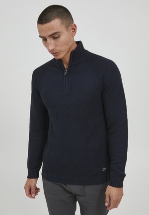 Mornarska zip-up dukserica s teksturiranim pletenim uzorkom, rebrastim ovratnikom i manžetama, te suptilnim logom blizu rubnog dijela.