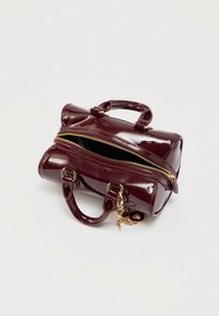 Sac à main en cuir verni bordeaux avec fermeture éclair dorée, deux poignées courtes, forme ovale et détail porte-clés. Fermeture éclair ouverte révélant l'intérieur.