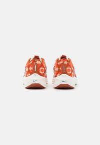 Buty sportowe z czerwono-białym kwiatowym wzorem, cholewką tekstylną, wyściełanym kołnierzem oraz białą podeszwą z niebieskim akcentem.