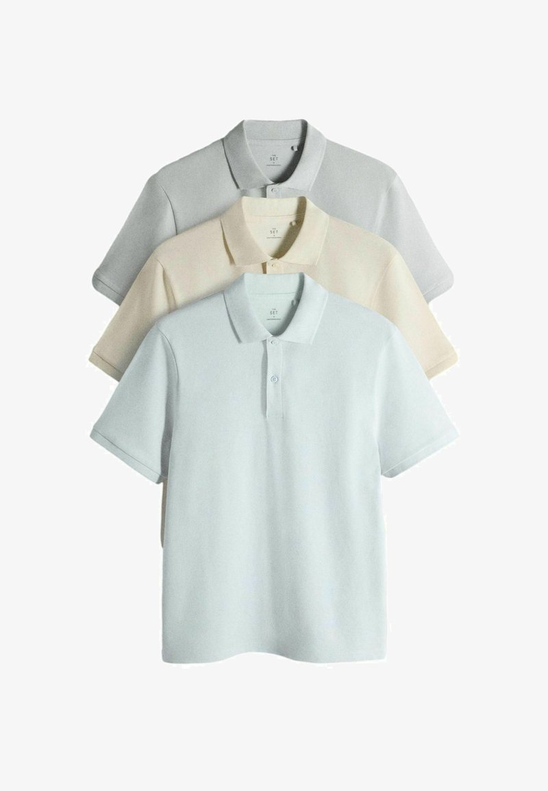 Tre polo a maniche corte impilate nei colori grigio chiaro, beige e azzurro pallido con colletto e due bottoni sul davanti.