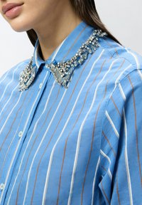 Camicia a maniche lunghe azzurra a righe con colletto ornato di argento, caratterizzata da dettagli intricati in perline e cristalli. Tessuto in cotone, vestibilità standard.