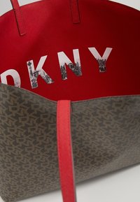Stort tote bag i mönstrat grått material med röd inredning där "DKNY" står i fet stil. Röda handtag för bärande.
