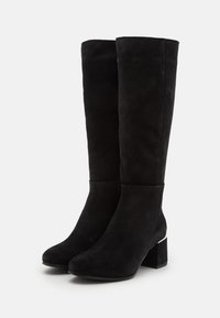 Botas negras hasta la rodilla, hechas de suave ante, con un tacón cuadrado y un acento metálico cerca del tacón. Textura suave, diseño elegante.