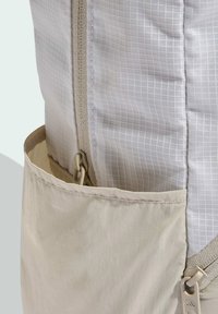 Zaino con tessuto a motivo a griglia bianca e una tasca beige. Cuciture rinforzate e dettaglio con clip per una chiusura sicura.