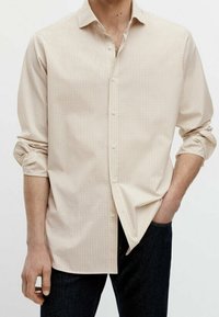 Chemise à carreaux beige clair avec un col boutonné, des manches longues retroussées jusqu'aux coudes et une coupe droite. Matière en coton, texture lisse.