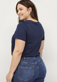 T-shirt blu navy a maniche corte con scollatura tonda, abbinato a jeans in denim blu con tasche posteriori e dettagli di cucitura discreti.