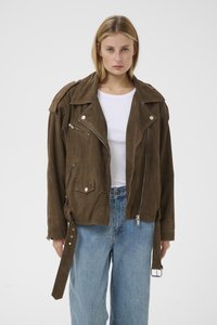 Bruine suède motorjack met grote kraag, zilveren ritssluitingen en zakken met drukknopen, gecombineerd met lichtgekleurde denim wijde pijpen jeans.