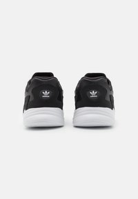 Sneaker Adidas neri con suole bianche viste da dietro, con il logo trefoil di Adidas su ogni tab di tallone.