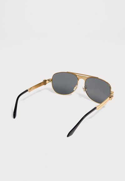 Γυαλιά ηλίου aviator με χρυσό σκελετό, σκούρους φακούς και μαύρα άκρα στα βραχίονες, σε λευκό φόντο.