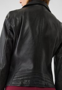Giubbotto in pelle nera con texture liscia, design strutturato e cuciture prominenti lungo le spalle e la schiena.