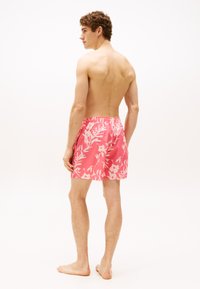 Bañadores rosas con patrones de hojas blancas, cinturilla elástica y bolsillos laterales, mostrados en un modelo sin camisa desde la espalda.
