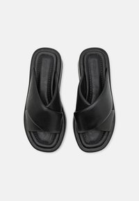 Sandales à glissière en cuir noir avec un design de lanières entrecroisées, semelle intérieure rembourrée et semelle texturée pour le confort. Profil plat sans matériel.