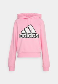 Sweat à capuche court rose en tissu doux, avec un logo Adidas noir et trois bandes blanches. Comprend une capuche à cordon de serrage et des poignets côtelés.