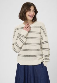 Tejfehér pulcsi szürke átlós csíkokkal, puha textúrával, kerek nyakkal és bordás mandzsettákkal, sötétkék farmerszoknyával párosítva.