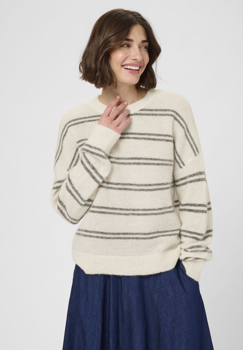 Tejfehér pulcsi szürke átlós csíkokkal, puha textúrával, kerek nyakkal és bordás mandzsettákkal, sötétkék farmerszoknyával párosítva.