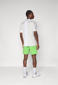 Graues Sportshirt mit weißen Akzenten, kombiniert mit hellgrünen Shorts. Mit kurzen Ärmeln und einer lockeren Passform entworfen, geeignet für den Sport.