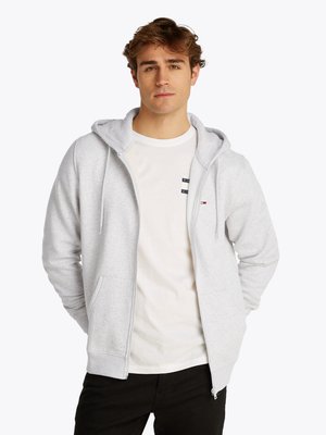 Grijze zip-up hoodie met een capuchon, voorzien van voorzakken en ribgebreide manchetten. Gedragen over een wit T-shirt met een klein logo detail.