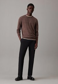 Maglione marrone con texture e collo a giro, abbinato a pantaloni neri slim-fit e scarpe nere lucide. Design semplice, senza motivi visibili.