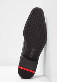 Black shoe sole with patterned tread, featuring a red accent band. Material appears rubber, designed for grip and durability.