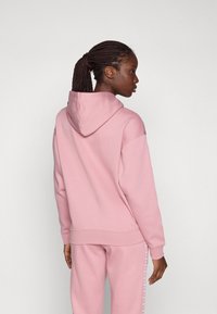 Rosa hettegenser med en avslappet passform, lange ermer og ribbestrikkede mansjetter. Vist er et baksidebilde som fremhever den myke stoffkvaliteten.