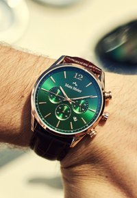 Montre chronographe avec un cadran dégradé vert, des accents en or rose, un bracelet en cuir marron et trois sous-cadrans ; affichage de la date à 6 heures.
