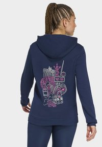 Kvinde med flettet hår iført en marineblå hættetrøje med et pink og hvidt Berlin-tema grafisk design, der inkluderer vartegn og maratonur.