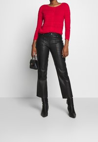 Cardigan rosso a coste con bottoni, abbinato a pantaloni neri a zampa corti in finta pelle. Borsa nera strutturata e stivaletti completano il look.