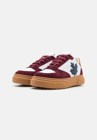 Zapatillas burdeos y blancas con material de ante, suela de goma y un acento en forma de hoja azul marino en el lado, con cordones planos y puntera perforada.