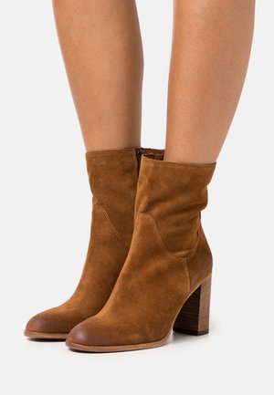 Braune Wildleder-Stiefeletten mit einem leicht lockeren Design, runder Zehenform und einem gestapelten Holzabsatz. Verfügt über einen seitlichen Reißverschluss für einfaches An- und Ausziehen.