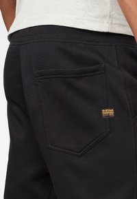 Svarta sweatpants i texturerat tyg med en bakficka och en liten guldloggobadge. Midjan är elastisk för komfort.