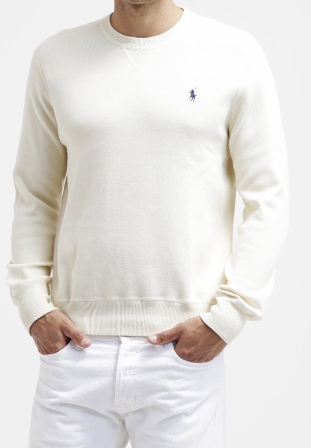 Kermanvärinen villapaita, joka on valmistettu teksturoidusta puuvillaneuleesta, siinä on pyöreä pääntie ja ribbausta helmassa, ja rinnassa on pieni sininen polo-logo.