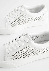 Weiße Sneaker mit perforierten Seitenpaneelen, flachen Schnürsenkeln, Gummisohlen und einer glatten Lederstruktur. Sauberes Design ohne sichtbares Branding.