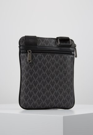 Sort crossbody taske med mønstret V-design, front lynlåslomme og justerbar strop spænde på en hvid piedestal.