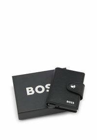 Zwarte lederen portemonnee met een gestructureerde afwerking, voorzien van een drukknoopsluiting en een zilveren logo-accent, geleverd met een zwarte doos.