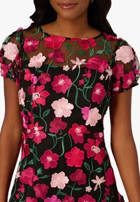 Černé šaty s výraznou vyšívkou květin v jasně růžové a světle růžové barvě na průsvitné vrstvě, s krátkými nafouknutými rukávy a kulatým výstřihem.