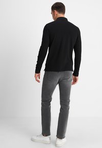 Polo nero a maniche lunghe con texture liscia, abbinato a jeans grigi slim-fit e sneakers bianche, visto da dietro.